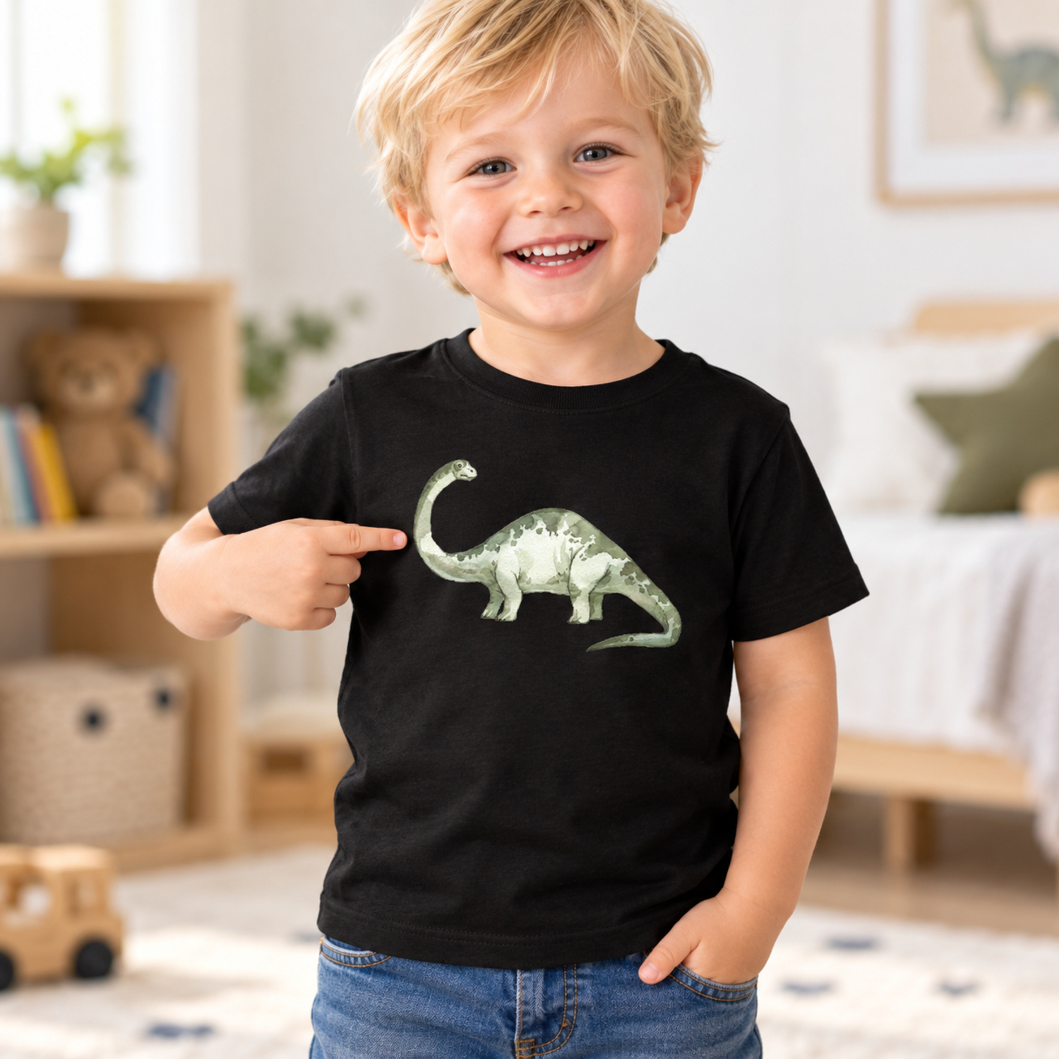 Usměvavý tříletý blonďatý chlapeček ukazuje na LaFi nažehlovačku zeleného dinosaura uprostřed černého trička – vizualizace.